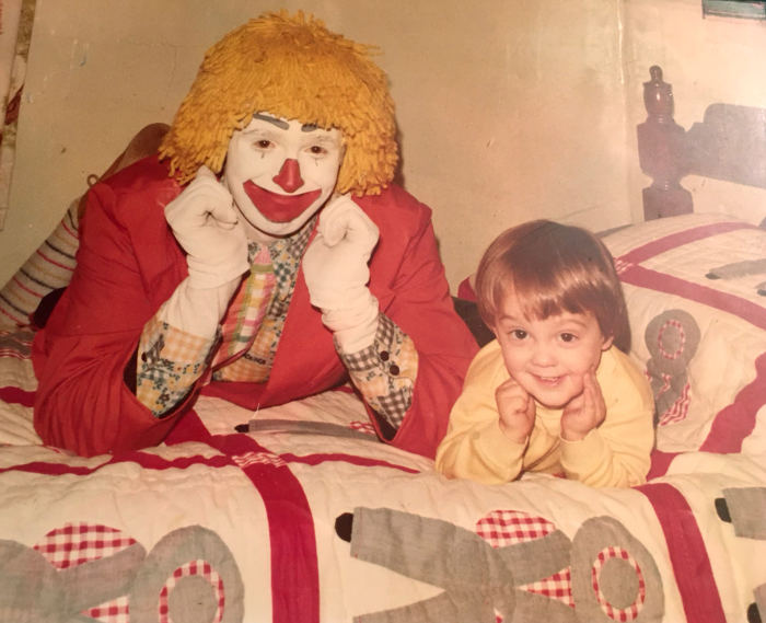 A vintage photo of a small child posing beside a clown.